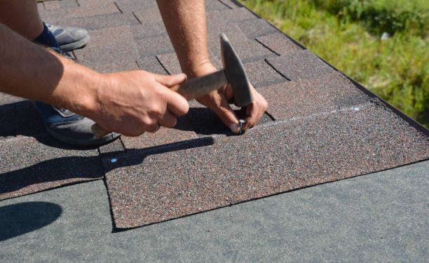 Roofer installing Asphalt Shingles on a house construction roof corner with a hammer and nails. Roofing construction with Asphalt Shingles.