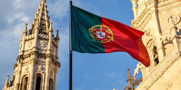 Portuguese flag waving in front of a blue sky and monastery